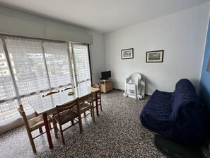 Ein Zimmer mit Esstisch, Stühlen, Fernseher, Sofa und zwei gerahmten Bildern an der Wand.