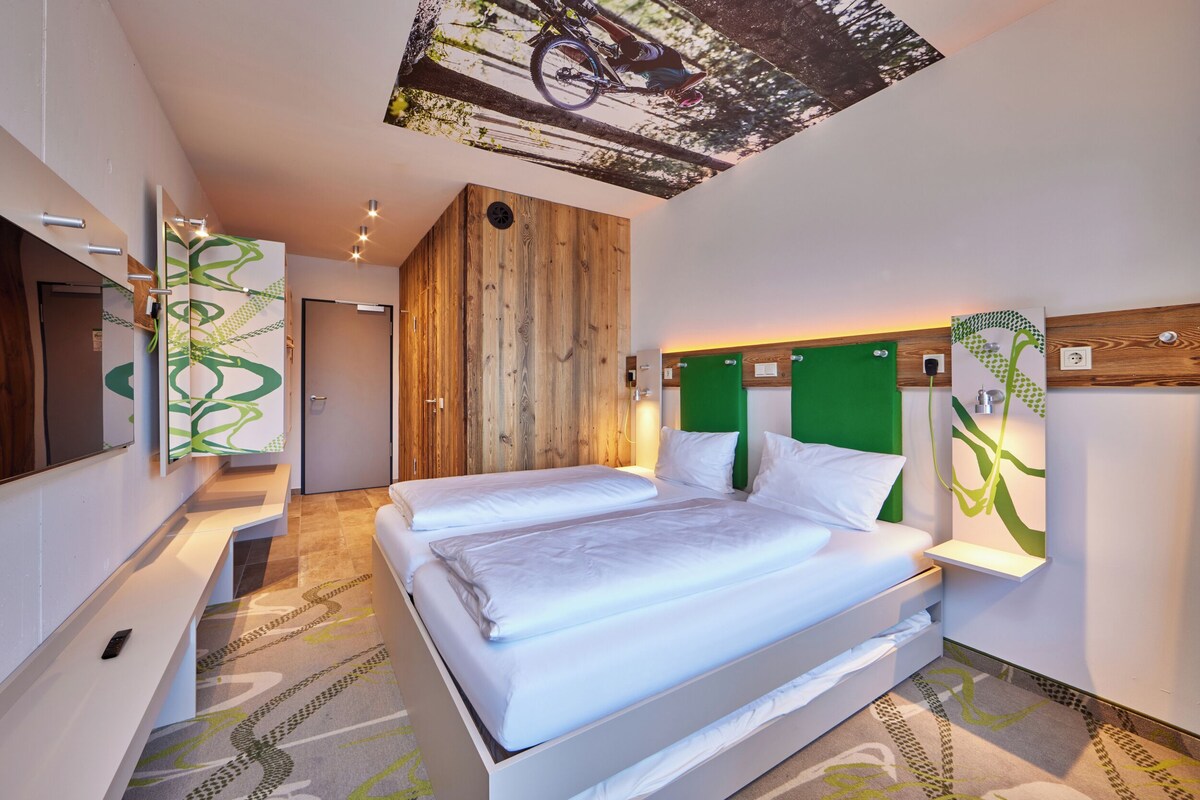 Une chambre d’hôtel moderne avec un grand lit, une télévision et un mur d’accent de couleur verte.
