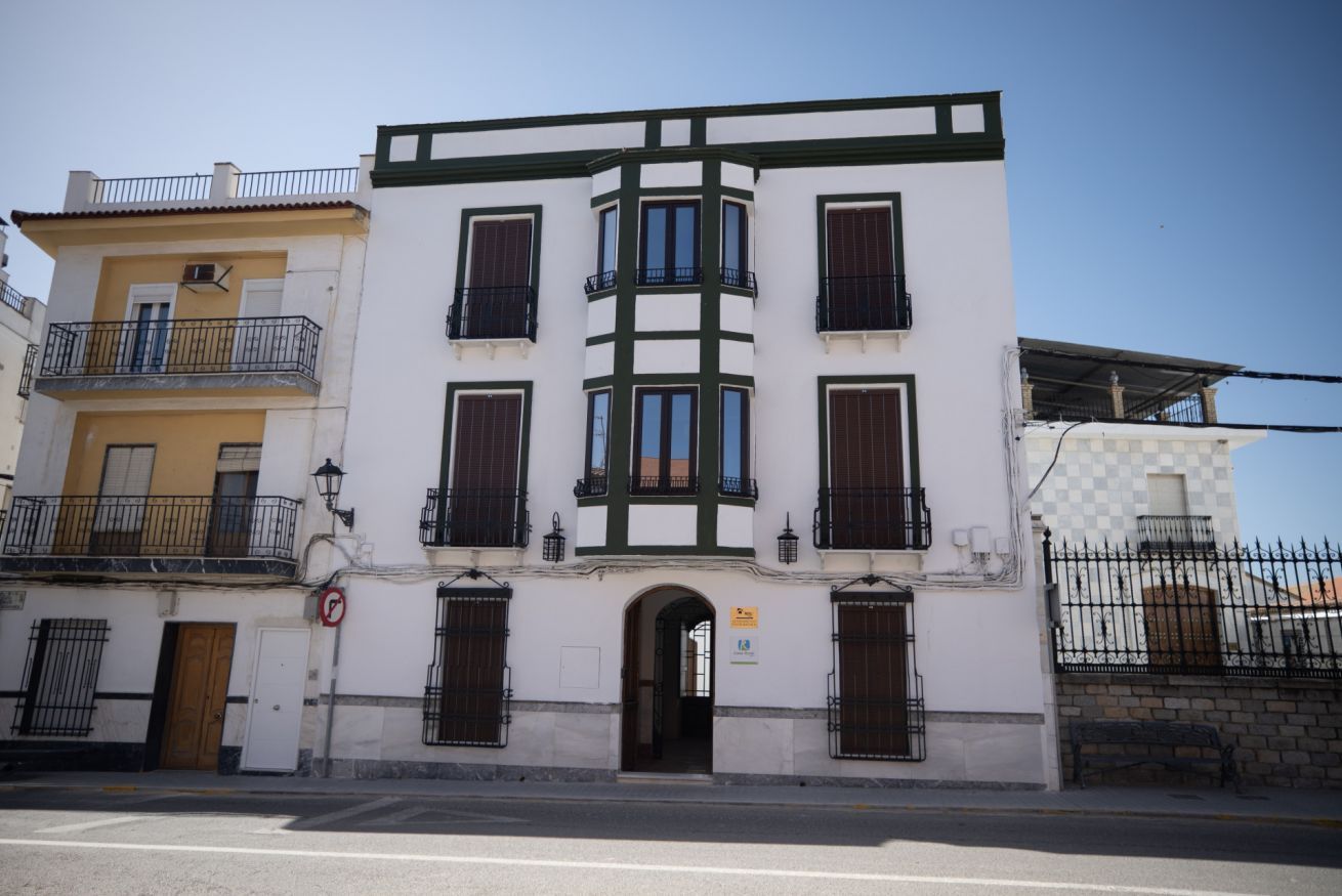Un edificio de varios pisos con una entrada central, balcones y fachada a cuadros.