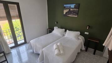 Habitación de hotel con dos camas, una pared verde, un cuadro y vista a través de un ventanal corredizo.