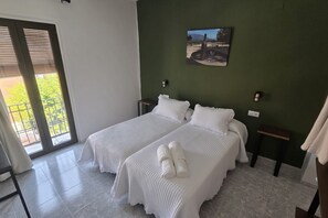 A hotel room with two beds, a green wall, a painting, and a view through a sliding door.