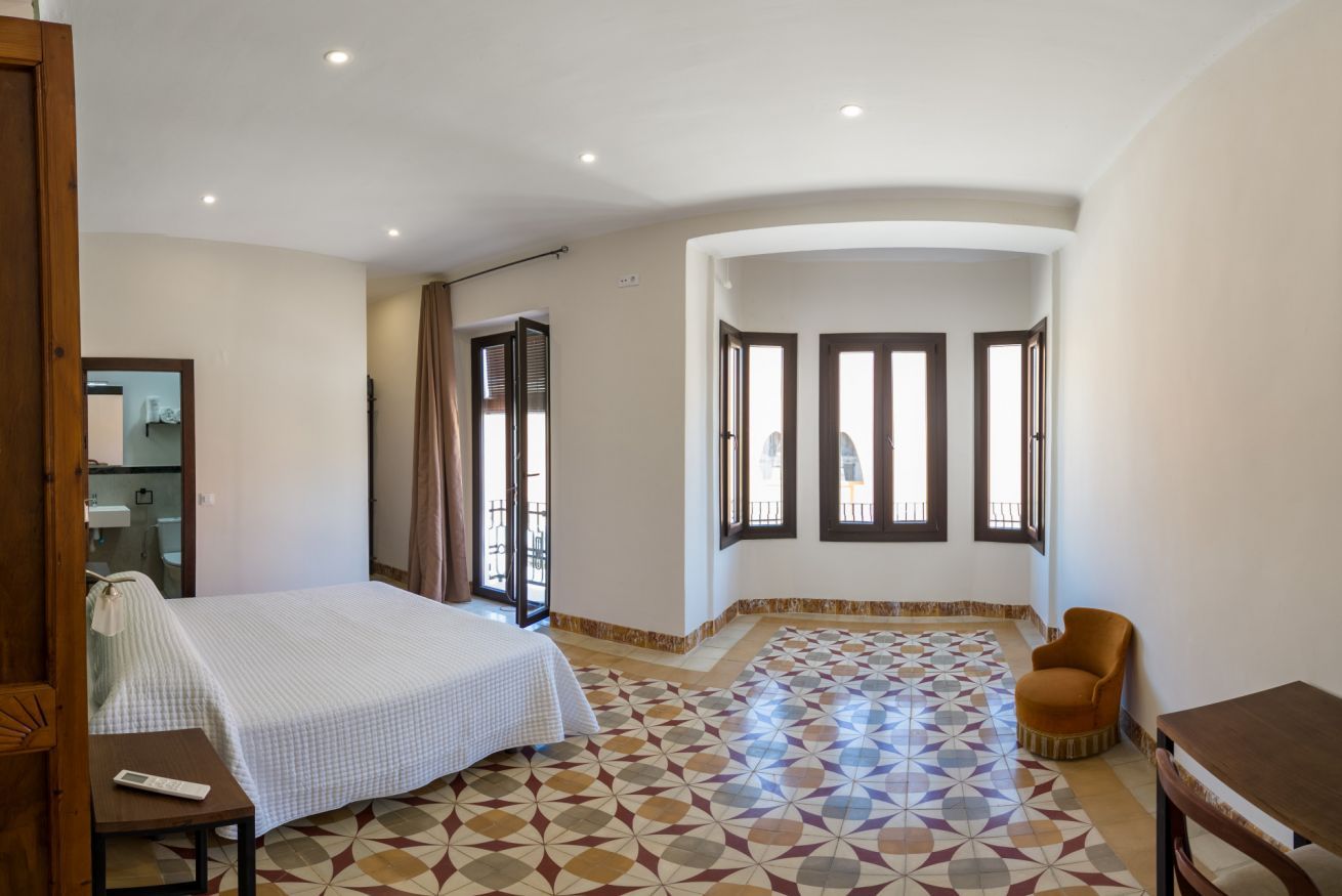 A bedroom with a bed, a chair, a table, and a window with a view.