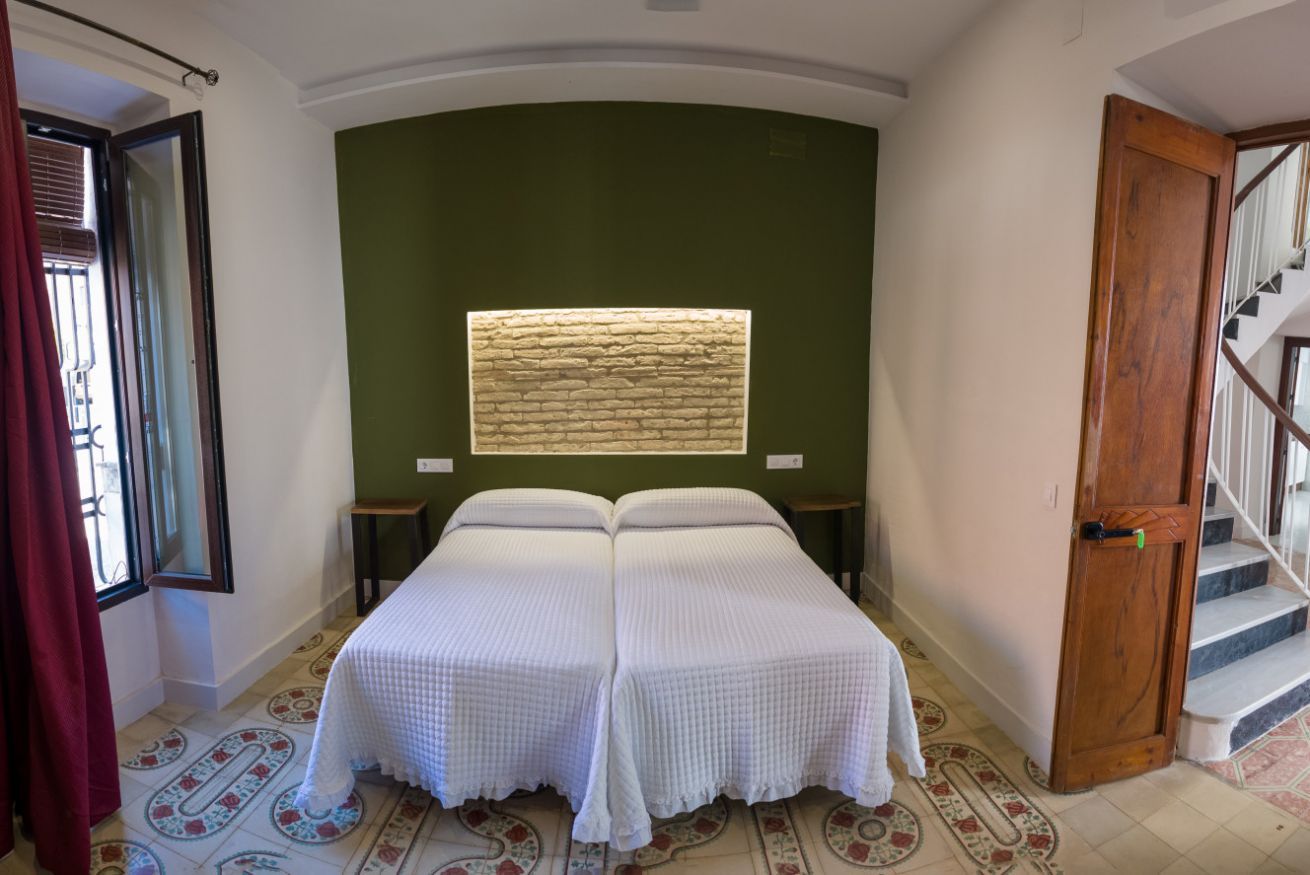 Una habitación con una cama, una ventana con pared texturizada, una escalera y una puerta.