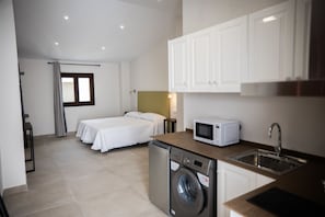 A compact hotel room with a bed, a washing machine, a microwave, and a sink.