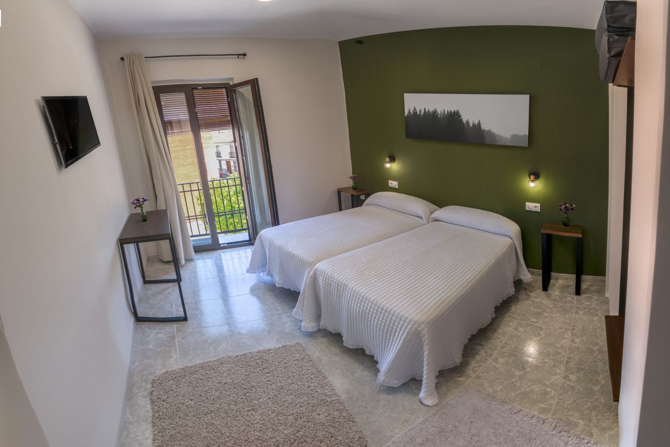 Ein Schlafzimmer mit zwei Betten, einem Fernseher, einem Gemälde und einem Balkon.
