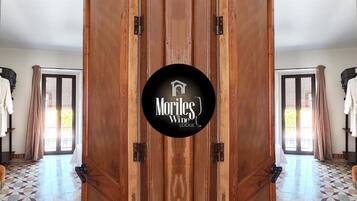 Eine Holztür mit dem Logo 'Moriles Wine Lodge' und Blick auf einen Raum mit gefliestem Boden und einem mit Vorhängen versehenen Fenster.