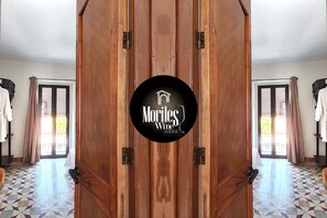 A wooden door with a logo for 'Moriles Wine Lodge' and a view of a room with a tiled floor and a window with curtains.