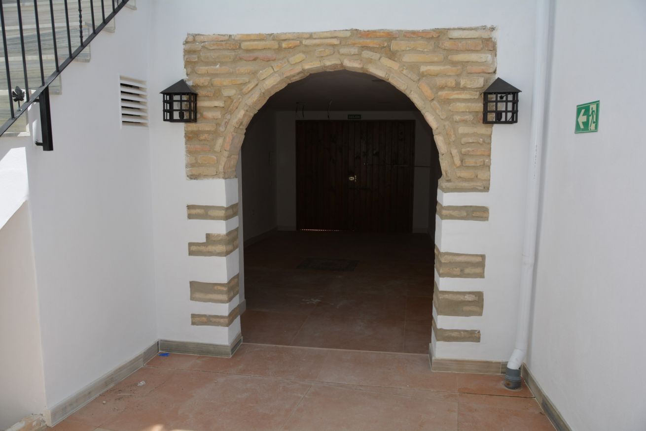 Ein steinerner Bogen führt in einen dunklen Innenraum mit einer sichtbaren Tür und einem grünen Hinweisschild an der Wand.