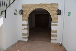 Un arco de piedra que da acceso a un espacio interior oscuro, con una puerta visible y un cartel direccional verde en la pared.