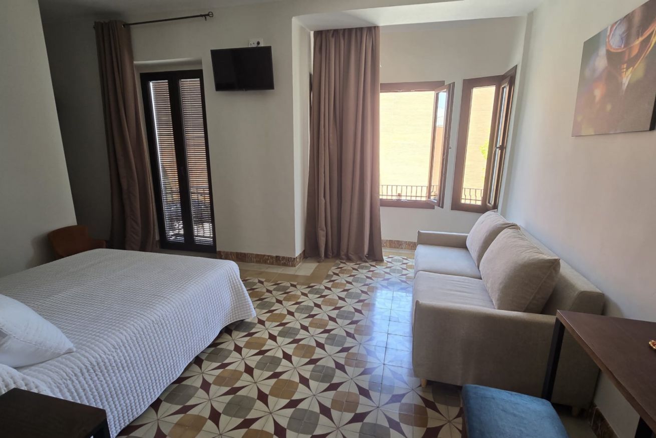 Una habitación de hotel con una cama, un sofá, una mesita y un televisor en la pared.