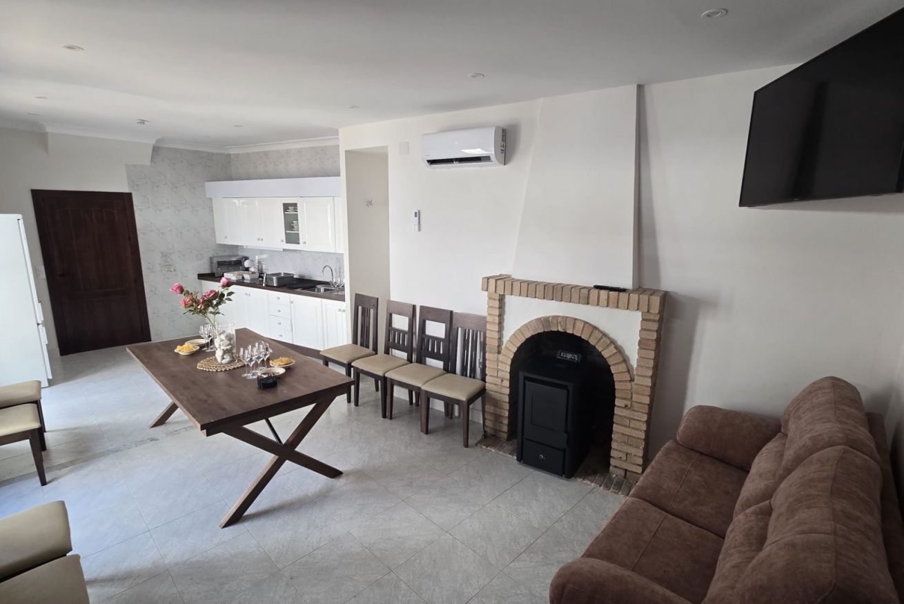 A modern living room with a fireplace, a dining area with a table set for four, and a kitchen in the background.