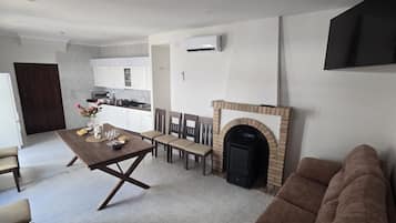 A modern living room with a fireplace, a dining area with a table set for four, and a kitchen in the background.