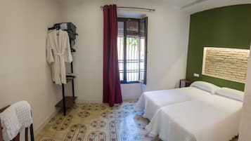 A room with two beds, a window with curtains, a towel rack, and a patterned floor.