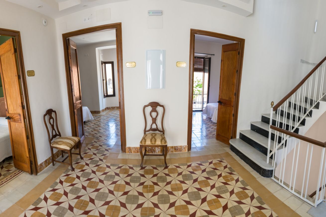 Un hall d’hôtel avec un sol à motifs, un banc en bois, un escalier et une vue sur l’extérieur.