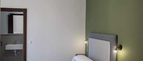 Une chambre d’hôtel comprenant un lit, une table de chevet, une lampe fixée au mur et une salle de bain avec un lavabo.