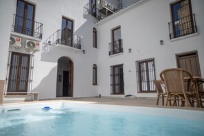 A courtyard with a swimming pool, outdoor seating, and a white building with multiple balconies.