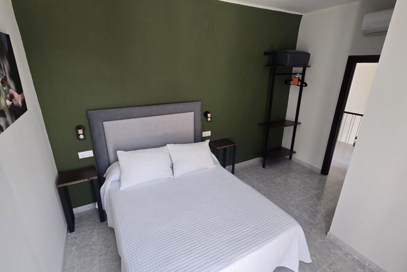 A bedroom with a bed, nightstands, a wall-mounted shelf, and a door.