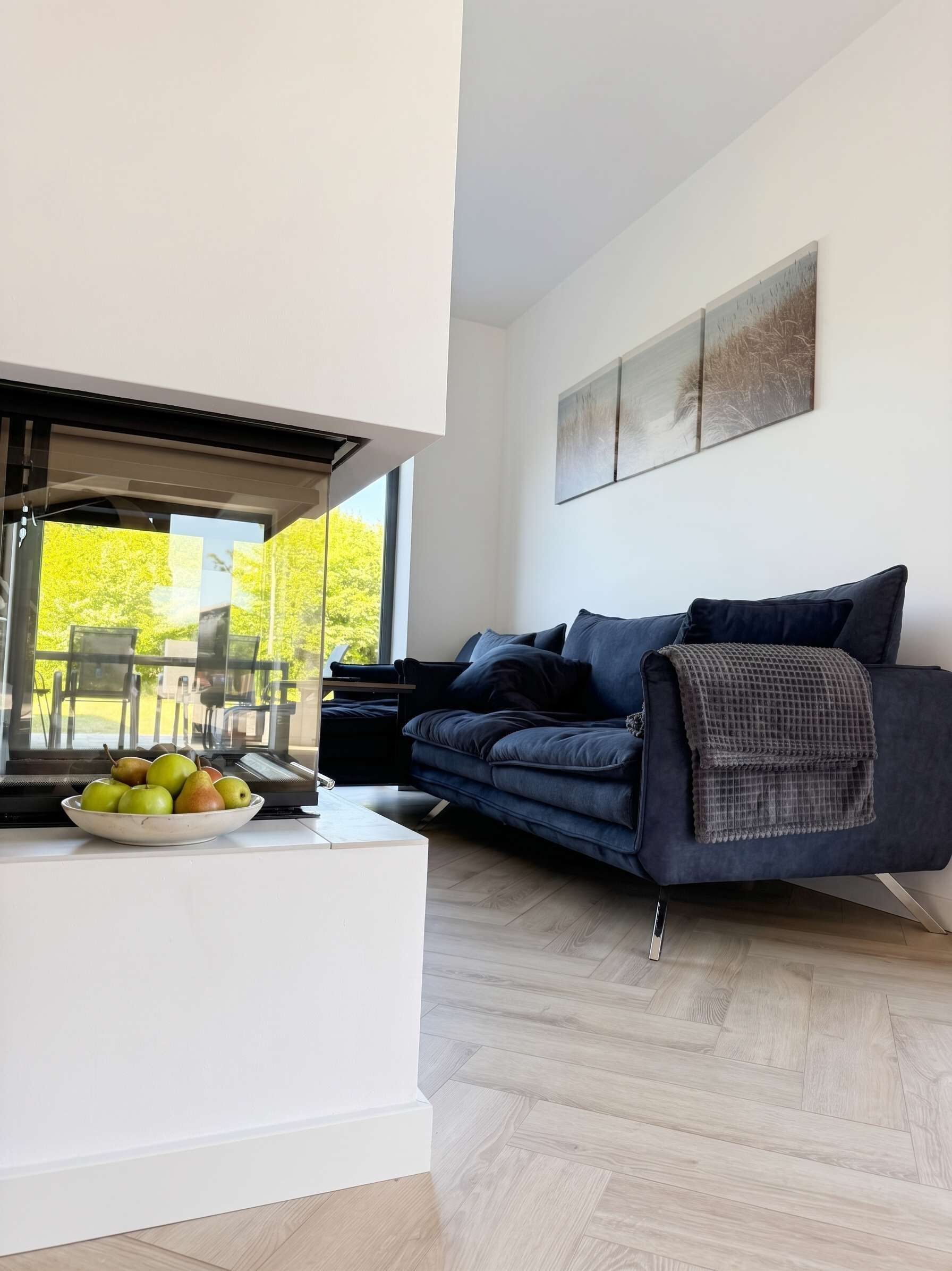 Een moderne woonkamer met een bank, een schaal fruit en een raam met uitzicht op een tuin.