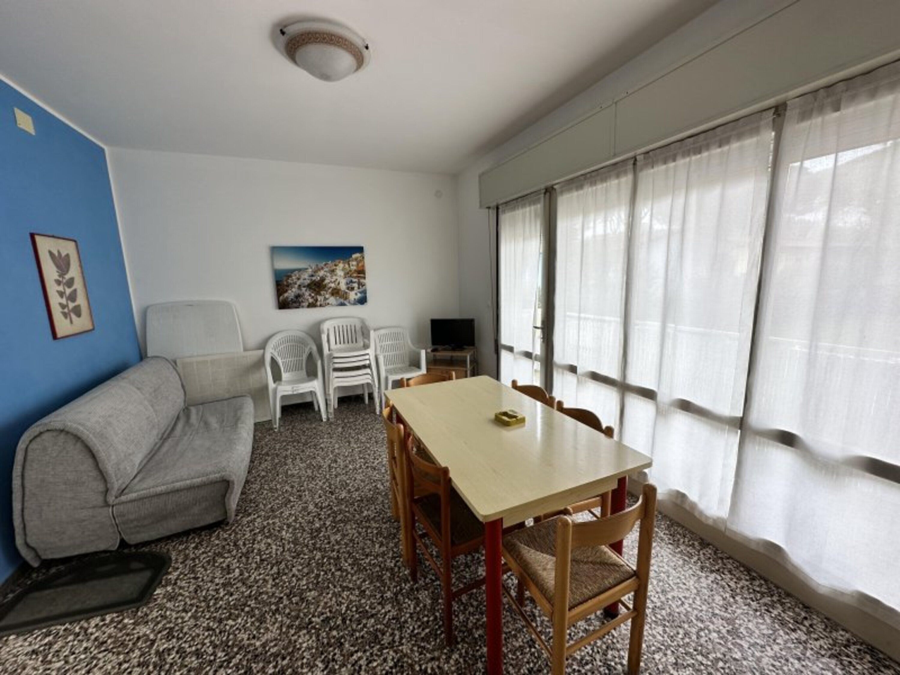 A room with a sofa, a table with chairs, a television, and a window with curtains.