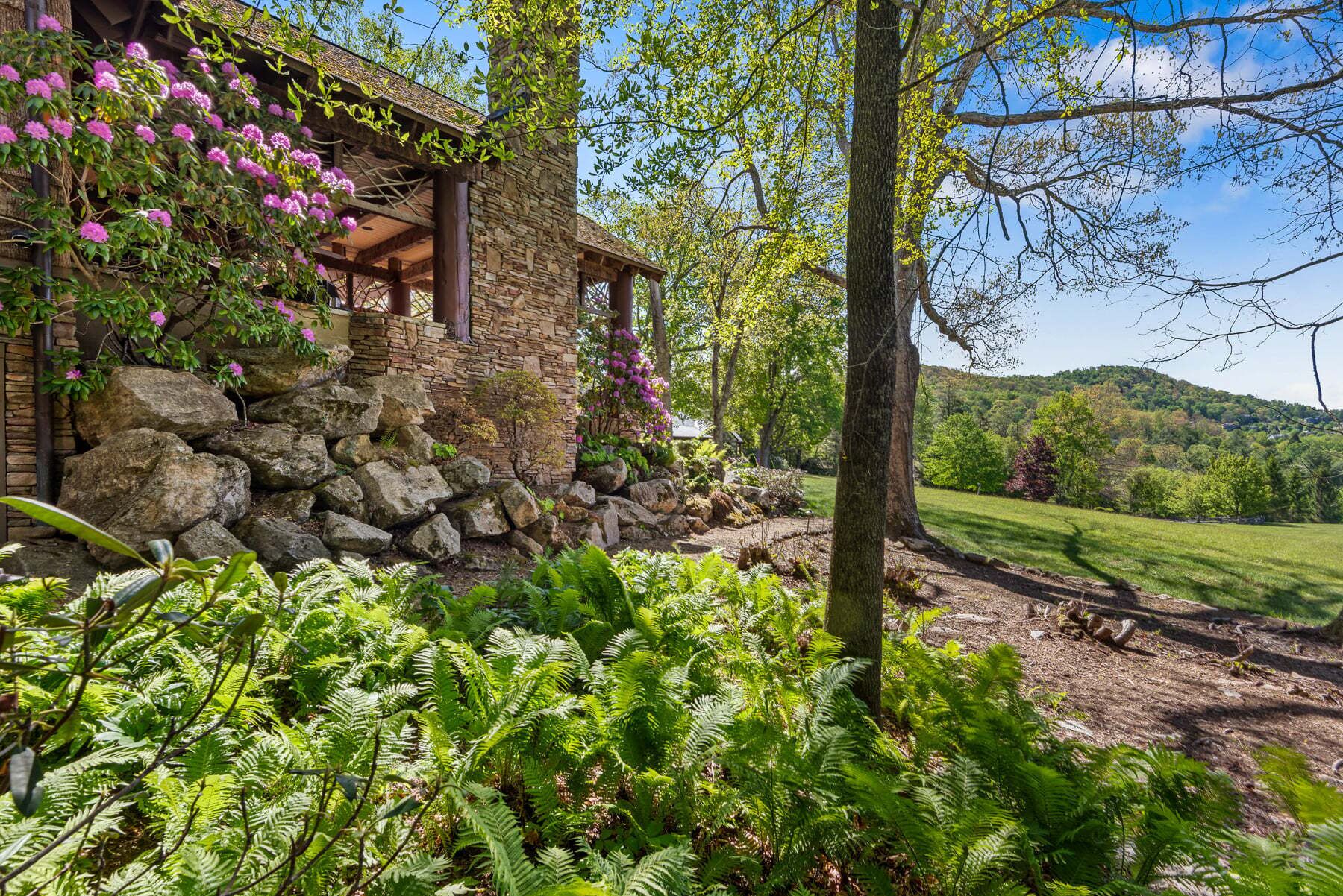 A stone building with a covered porch, surrounded by lush greenery and ferns.