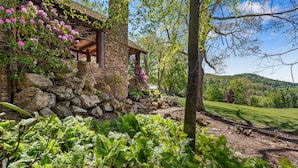 A stone building with a covered porch, surrounded by lush greenery and ferns. - Farm Hollow - luxury home with hot tub, covered fireplace (Banner Elk)