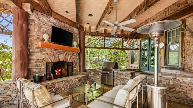 A stone fireplace, outdoor seating, a grill, and a ceiling fan in a rustic outdoor area. - Farm Hollow - luxury home with hot tub, covered fireplace (Banner Elk)