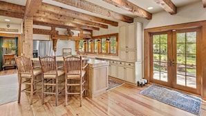 A rustic kitchen with wooden beams, a farmhouse-style dining area, and large windows. - Farm Hollow - luxury home with hot tub, covered fireplace (Banner Elk)