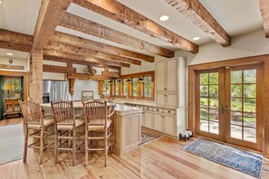 Eine rustikale Küche mit Holzbalken, einem Essbereich im Bauernhausstil und großen Fenstern.