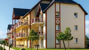 A multi-story hotel with balconies, a grassy lawn, and a wooden fence. - Stylish Coastal Apartment With Shared Pool (Frehel)