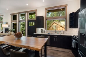 Eine moderne Küche mit großen Fenstern, einem Essbereich und Blick auf eine Holzhütte.