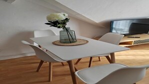 A dining area with a white table, white chairs, a vase with flowers, and a television on a wooden stand. - 200 m plage - Rue piétonne à 300 m - jardin (Berck)
