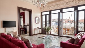 Ein Wohnzimmer mit Fernseher, roten Sofas, einem Glastisch und einem Balkon mit Blick auf Gebäude.