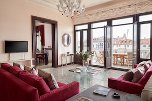 A living room with a TV, red sofas, a glass coffee table, and a balcony with a view of buildings. - Venice Prestige - Celestina on the Grand Canal R&R (Venice)