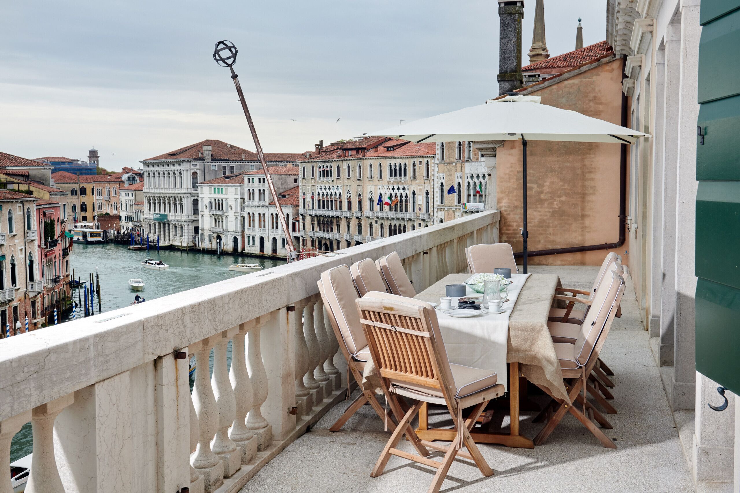 Un balcon avec une table dressée pour le dîner, donnant sur un canal bordé de bâtiments historiques et de bateaux.