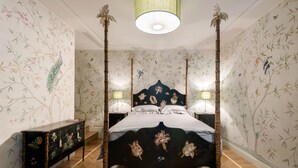 Ein Bett mit Baldachin, eine Blumendecke, ein Nachttisch mit Lampe und eine Kommode mit floralem Dekor.
