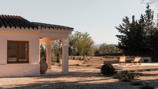 Un bâtiment doté d’un toit recouvert de tuiles, d’une grande fenêtre et d’un patio aménagé avec des chaises.