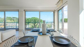 A modern dining area with a table set for four, large windows with a view of greenery and buildings, and a balcony with a railing. - Rome From Above - Apt With a View (Rome)