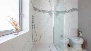 A bathroom with a glass shower enclosure, a toilet, and a window with a vase of dried flowers. - Rome From Above - Apt With a View (Rome)