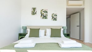 A neatly made bed with green and white pillows, a green throw blanket, and two white towels on the bed.