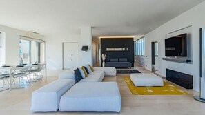 A modern living room with a sofa set, a dining area with chairs, a TV mounted on the wall, and a fireplace. - Rome From Above - Apt With a View (Rome)