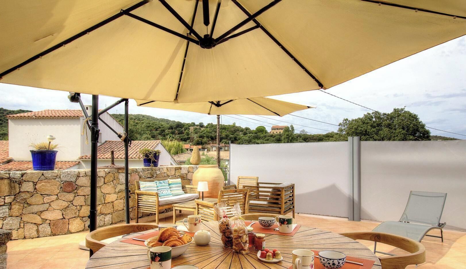 Un patio exterior con una mesa, sillas, un gran toldo y un muro de piedra.