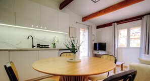Une cuisine moderne avec des meubles blancs, une table de salle à manger ronde en bois et un téléviseur en arrière-plan.