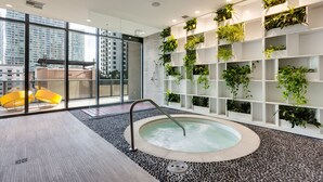 A modern indoor pool with a jacuzzi, surrounded by a pebble floor, and a wall with shelves of plants. - Brickell Heights High-Floor Suite with King Bed, Den, 2 Baths, Skyline Views (Miami)