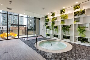Ein moderner Innenpool mit Whirlpool, umgeben von einem Kieselboden und einer Wand mit Pflanzenregalen.