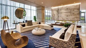 A modern living room with a sectional sofa, a round coffee table, a large mirror, and a marble wall. - Brickell Heights High-Floor Suite with King Bed, Den, 2 Baths, Skyline Views (Miami)