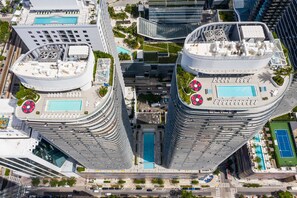 Ein Hochhaus mit Pool auf dem Dach, Tennisplatz und einer begrünten Anlage mit Palmen.