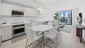 A modern kitchen with white cabinets, a microwave, and an oven. There is a dining area with a white table and chairs. - Brickell Heights High-Floor Suite with King Bed, Den, 2 Baths, Skyline Views (Miami)