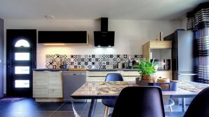 Una cucina moderna con zona pranzo, pensili e basi nere, cappa aspirante nera, zoccolo decorato e una pianta in vaso.