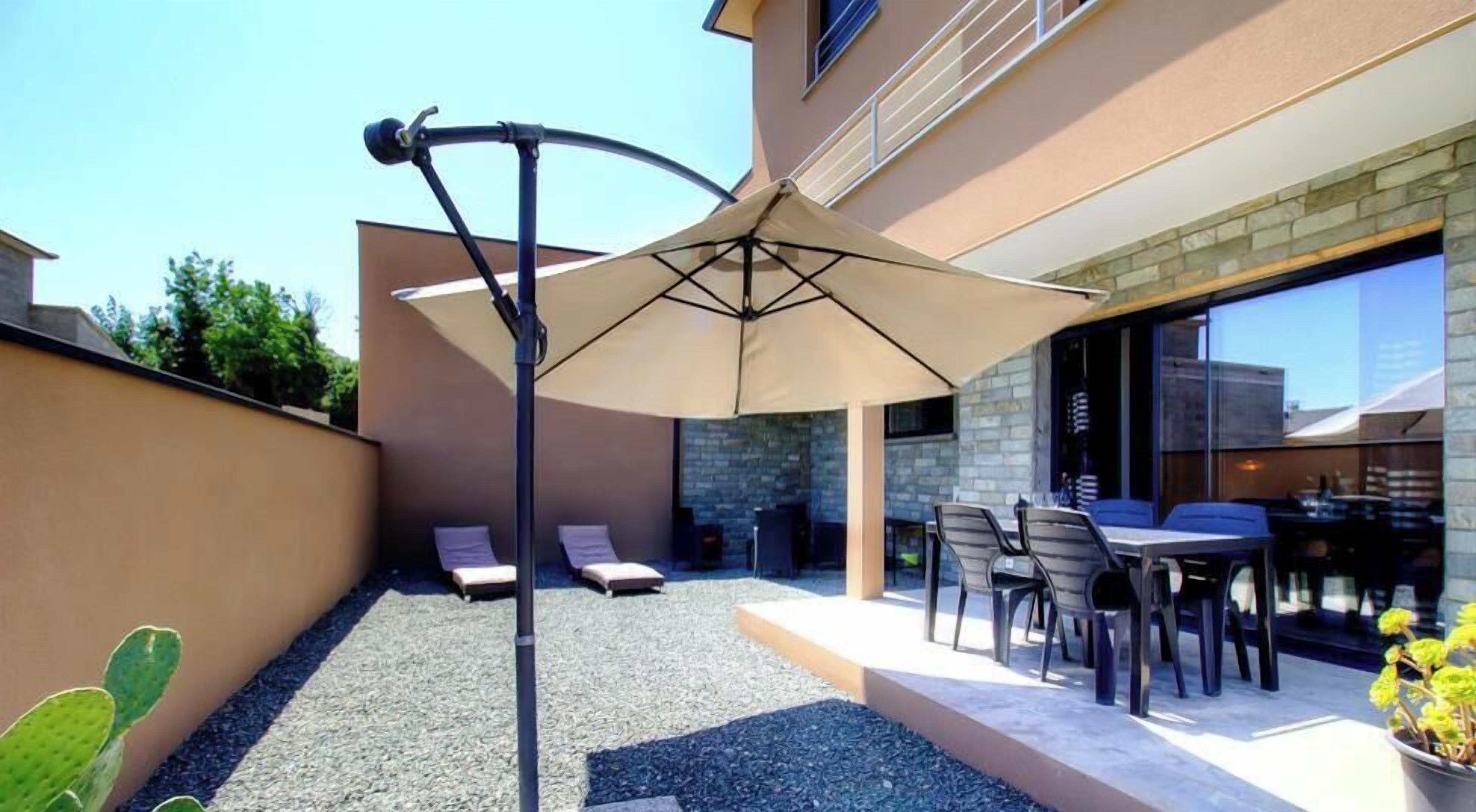 A patio with a table and chairs, a large umbrella, and two lounge chairs.