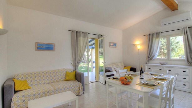 A room with a sofa, dining table, chairs, and a view through a glass door. - Casetta des Oliviers (SARTENE)